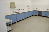 Stół laboratoryjny przyścienny ze zlewem, szafkami i miejscem do siedzenia.